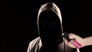 Attacker in the dark with hoodie covering face and woman's hand with a pink lipstick stun gun