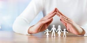 Woman's hands forming a roof over a paper family representing Home security and personal safety for the family