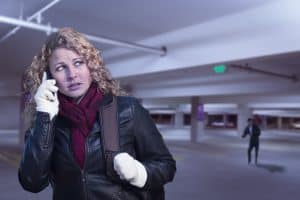 Woman in a garage with someone following her while she is on her phone wearing gloves